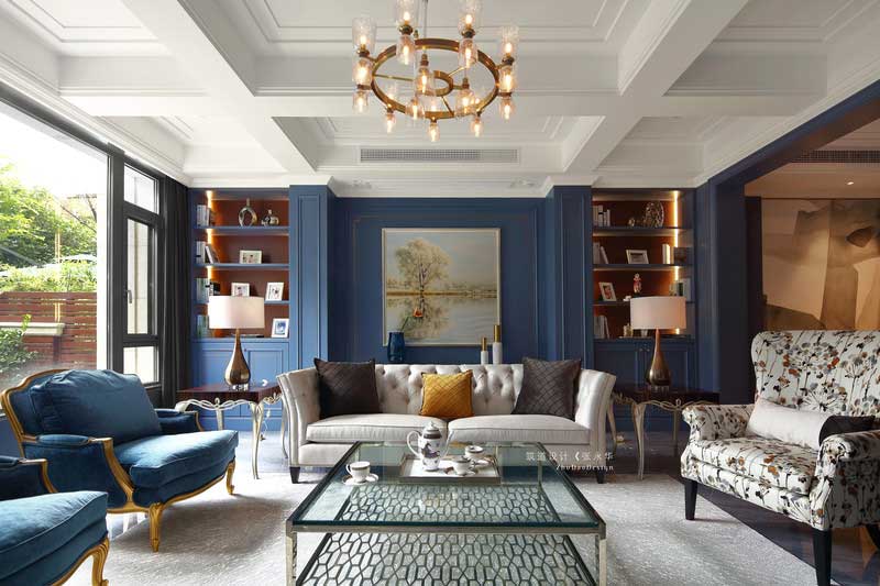 客廳的立面有兩處裝飾柜，兩面相對稱呼應。裝飾上運用涂料和護墻的手法，使空間豐富感更強。深灰色地磚一鋪到底，從客廳一直延伸到餐廳，并鋪上米灰色地毯做裝飾，使空間色彩更加柔和。