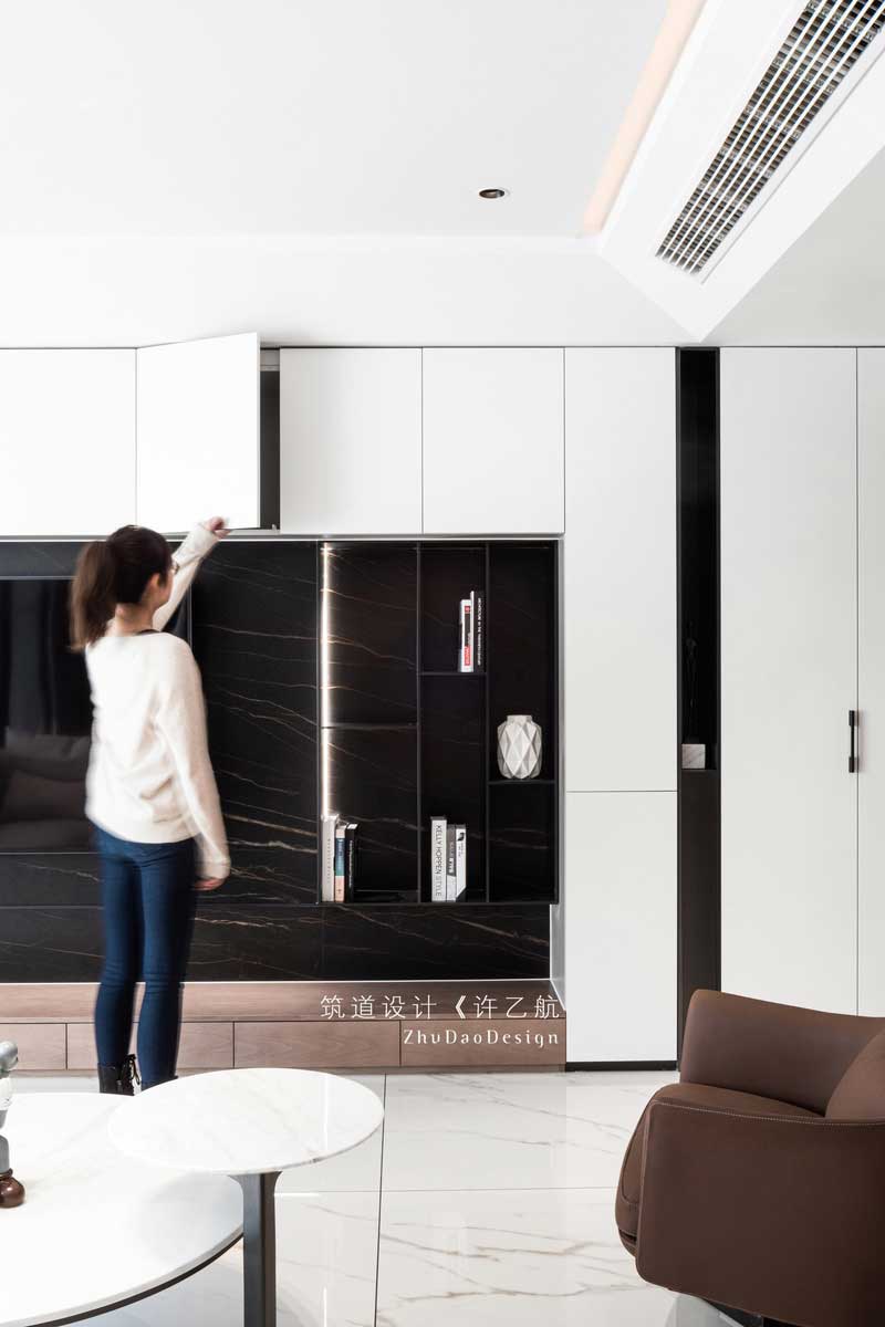  設計師拋棄傳統客廳的固有印象，將儲物柜與電視背景墻相結合，不僅增加了空間的儲物空間，在自然柔和的燈帶的襯托下，深灰色的啞光金屬條與深色大理石背景更有層次感，也成為了公共空間的一亮點所在。